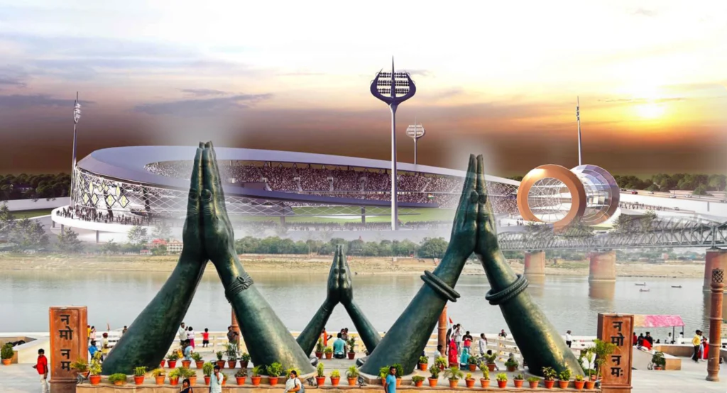 Large folded-hands sculptures overlooking a river, with a modern stadium and bridge at sunset.
